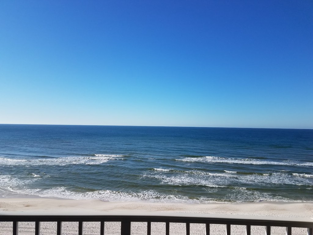 Quiet Gulf waves and an empty white-sand beach viewed from a balcony in Panama City Beach